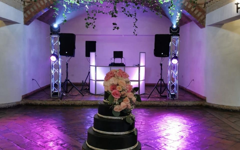 Salón de boda decorado con torta y montaje de DJ al fondo