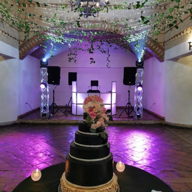 Salón de boda decorado con torta y montaje de DJ al fondo